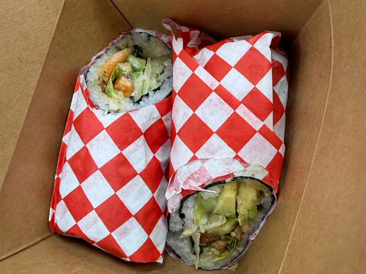 Two sushi burritos wrapped in red checkered paper inside a takeout box