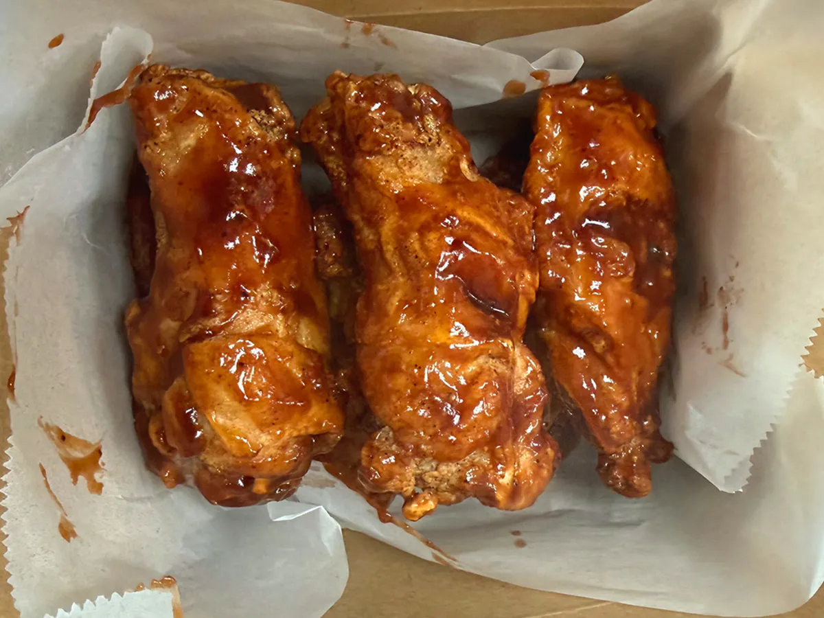 Three glazed chicken wings served in a takeout container