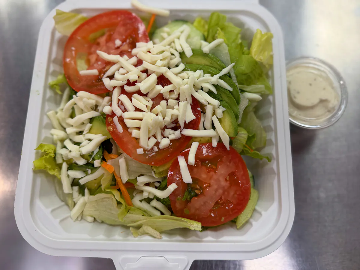 Fresh garden salad with lettuce, tomato, avocado, shredded cheese, and dressing